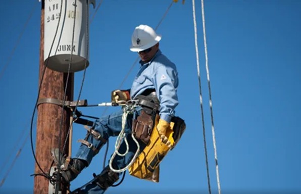 Utility worker wearing FR-rated workwear and safety gear while performing maintenance on a power line.