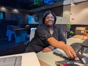 Sherhonda assisting a client call at the Feury Image Group service desk in NJ. Description: At the Feury Image Group front desk, Sherhonda answers client inquiries with a personal touch — representing the responsive, relationship-driven service that defines Work Hard Dress Right.