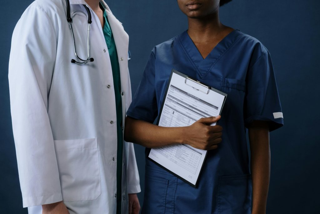 Healthcare professionals wearing a white lab coat and blue scrubs stand side by side, highlighting coordinated medical uniforms from Work Hard Dress Right