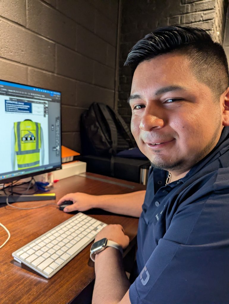 Feury Image Group graphic artist reviewing branded safety vest artwork on computer screen using Adobe Illustrator for print production.