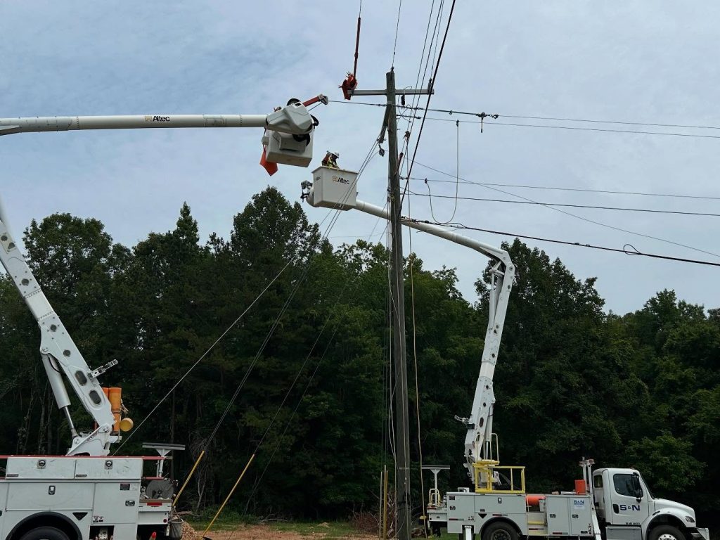 Utility crews in bucket trucks wearing FR clothing repair overhead power lines on a utility pole.