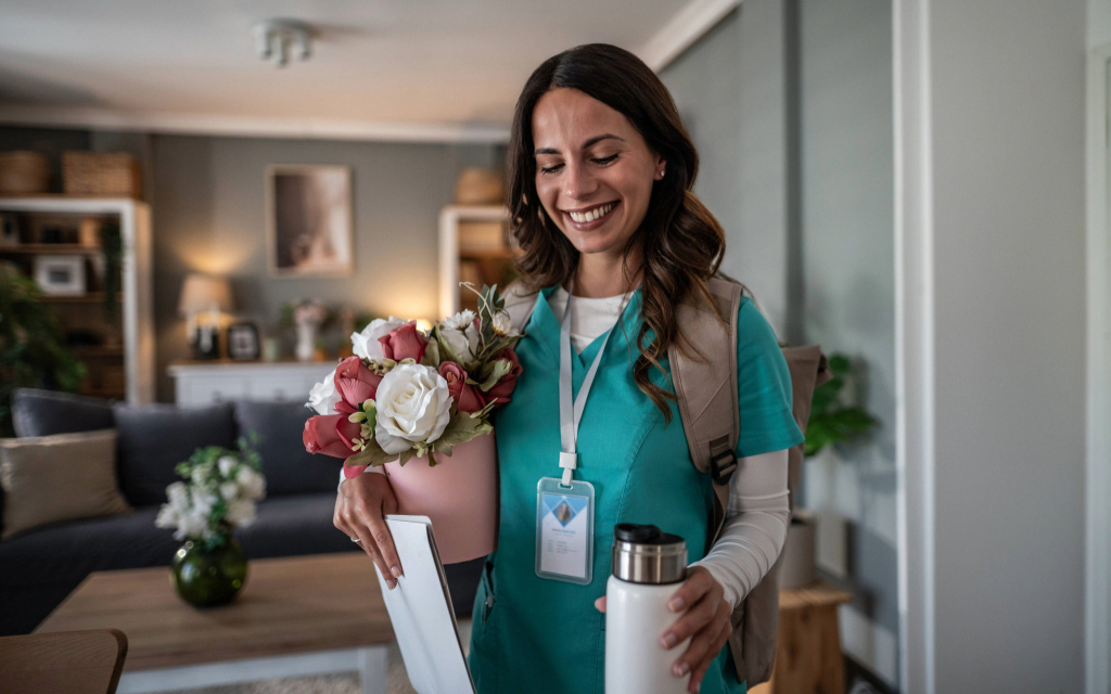 A nurse smiles in her living room, thankful for her employer’s gift ideas for National Nurses Day.