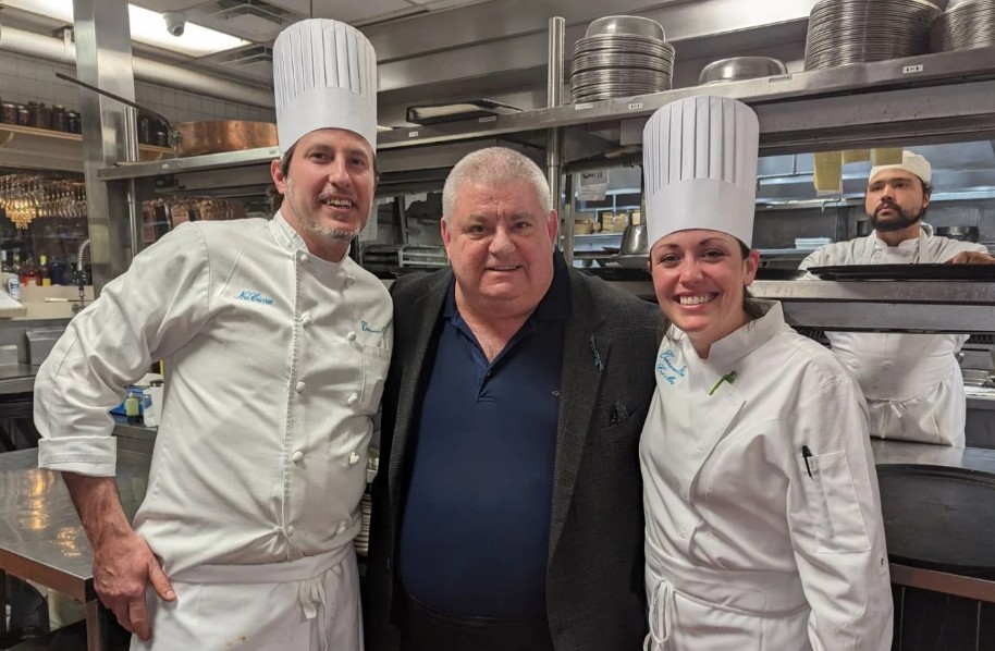 Chef Cardie Mortimer with chefs wearing professional chef uniforms and hats in a commercial kitchen