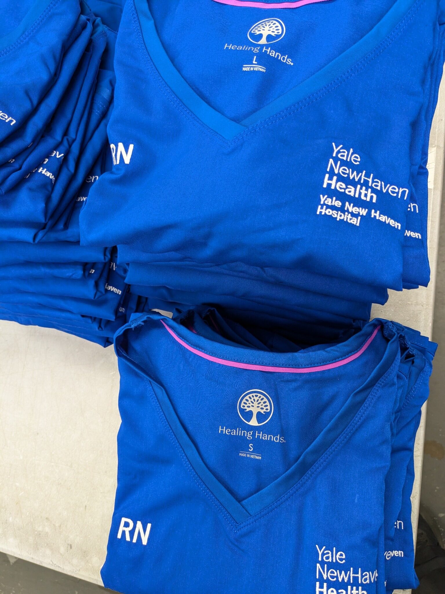 Multiple embroidered healthcare scrub tops prepared for an employee uniform program