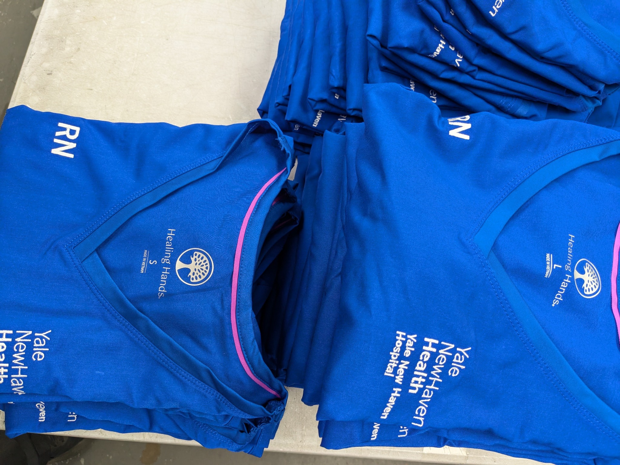 Multiple embroidered healthcare scrub tops prepared for an employee uniform program